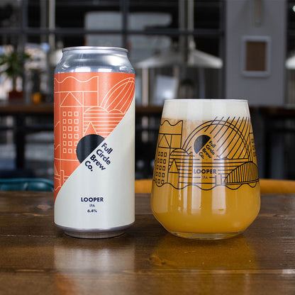 A lifestyle photograph of a can of Looper IPA alongside the craft beer poured into an Allegre glass on a wooden bar table top.